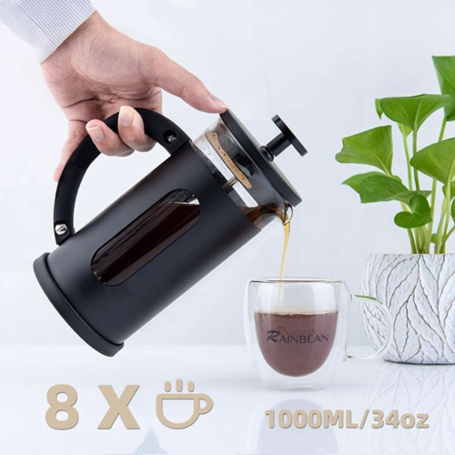 Person pouring coffee from a black French press into a glass mug on a light background with a plant.